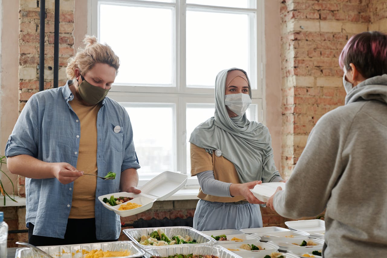 Volunteers wearing masks distribute meals indoors, promoting safety and care.